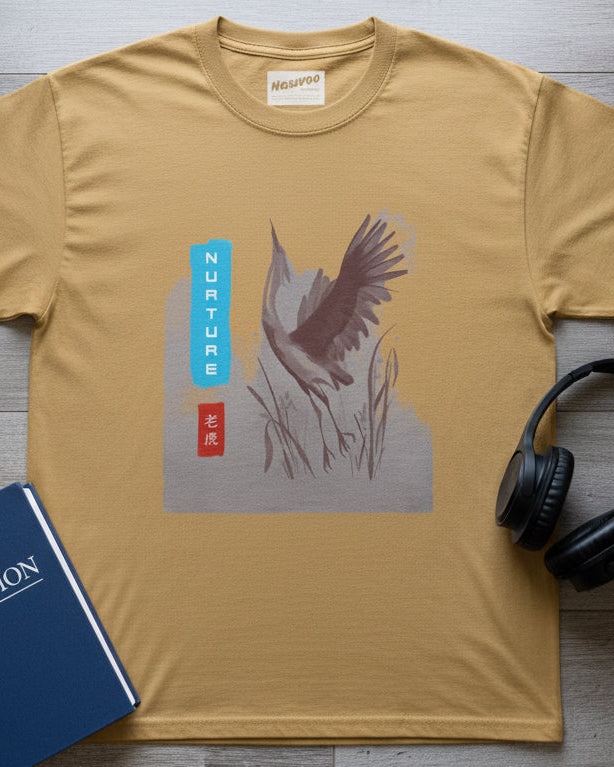 A mustard yellow short-sleeve t-shirt with a central graphic print of a flying bird in gray and brown, next to a vertical blue and red label with white text, displayed on a solid white background.