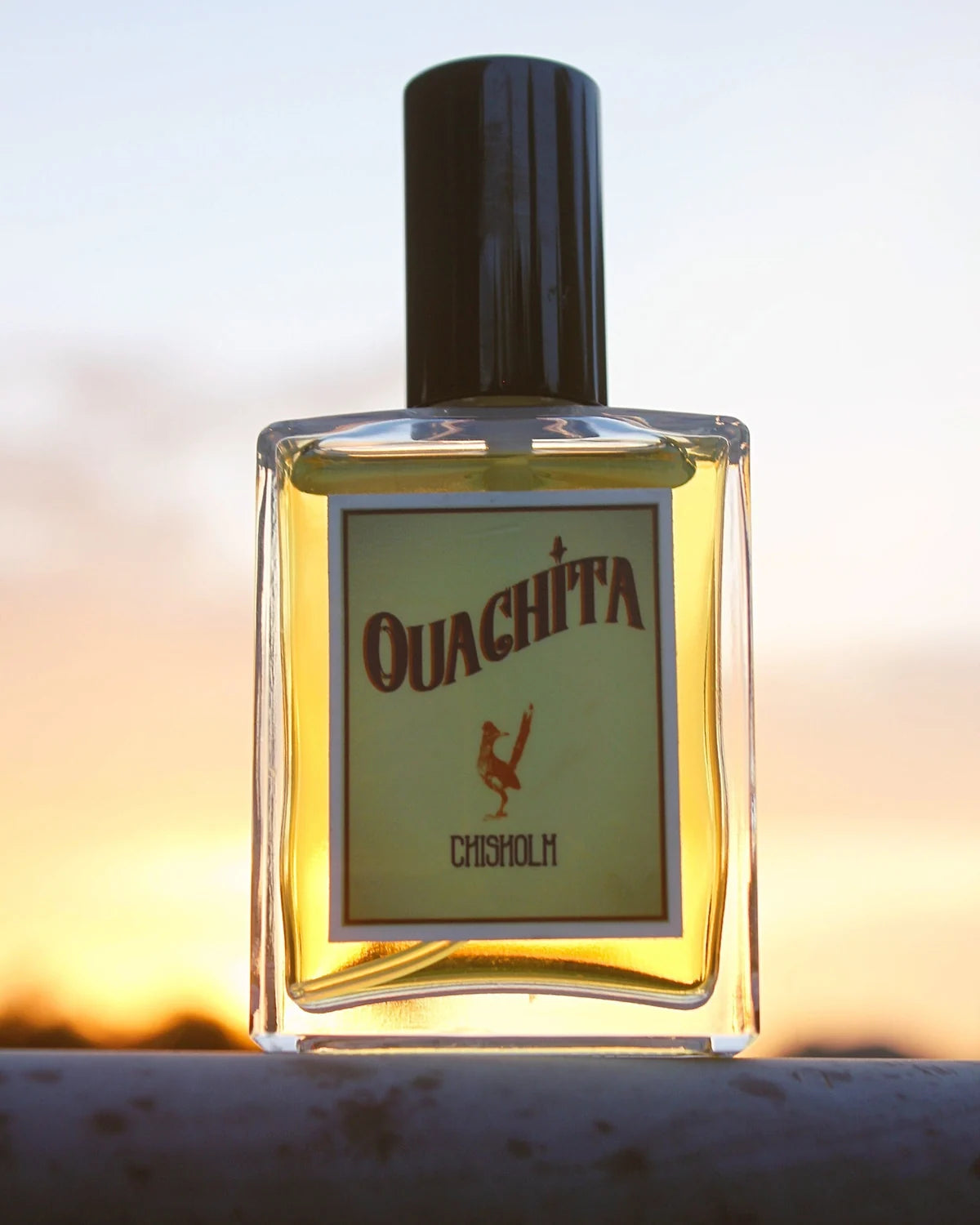 A bottle of Ouachita Chisholm cologne, backlit by a sunset.
