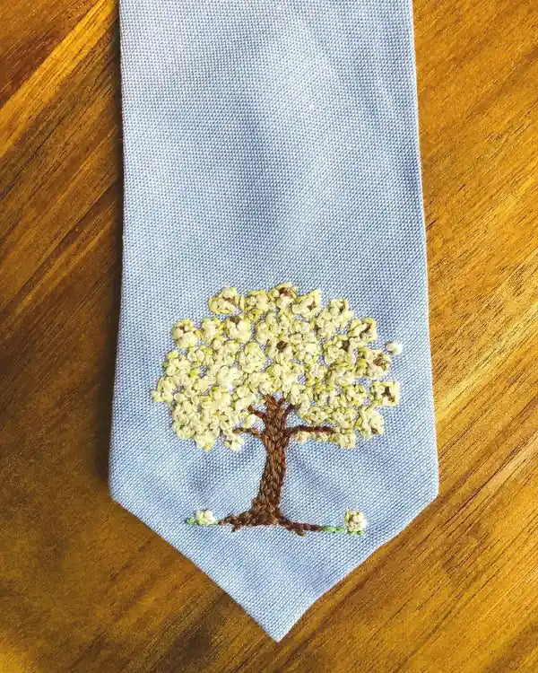 A light blue necktie hand-embroidered with a tree in full popcorn-white blossom.